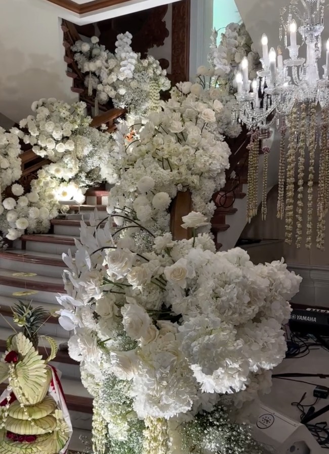 Tangga utama rumah tampak dipenuhi dengan bunga-bunga berwarna putih. Tangga tersebut menjadi latar belakang dari tempat ijab kabul Uta dan Andie. Perpaduan nuansa Bali terlihat dalam beberapa dekorasi yang turut menghiasi. Foto: Instagram/@bimo_singgih