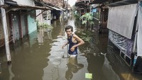 Warga melintas di depan rumahnya yang terendam banjir.