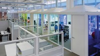Ada ruangan tertutup dengan kaca berwarna biru dan hijau dipadukan dengan pintu dan kusen warna putih. Sementara itu, di luar ruangan tersebut juga ada meja kubikal.