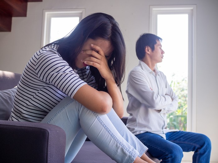 Ilustrasi suami istri Asian couple have serious quarrel problems sitting on the sofa inside the house. the wife bowed sad. The husband turned his back after a conflict.