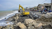 Operator menggunakan alat berat membuat tanggul penahan ombak.  