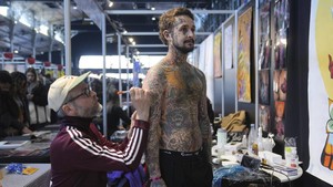 Seorang seniman tato menggambar dasar tato di lengan seorang pria selama konvensi tato di Paris, Minggu (2/2/2025).  