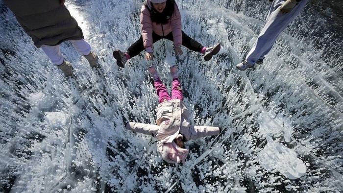 Warga China Nikmati Fenomena Gelembung Danau yang Membeku A woman has fun with a child on a frozen lake at a mountain scenic area during a week-long Chinese New Year holiday, in Miyun, north of Beijing on Sunday, Feb. 2, 2025. (AP Photo/Andy Wong)