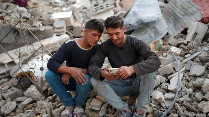 Dipisahkan Perang, Saudara Kembar Ini Bertemu di Rumah Mereka yang Hancur Palestinian twins Mahmoud and Ibrahim Al-Atout, who were separated during the war when Ibrahim was displaced to the southern part of Gaza at Israel's order, carry a table as they search for belongings through the rubble of their destroyed house after being reunited, in Jabalia, northern Gaza Strip, January 29, 2025. REUTERS/Osama Al-Arabid