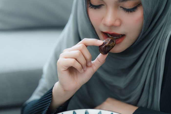 Muslim woman in hijab eating dates fruit in a comfortable home. Clouse up shot