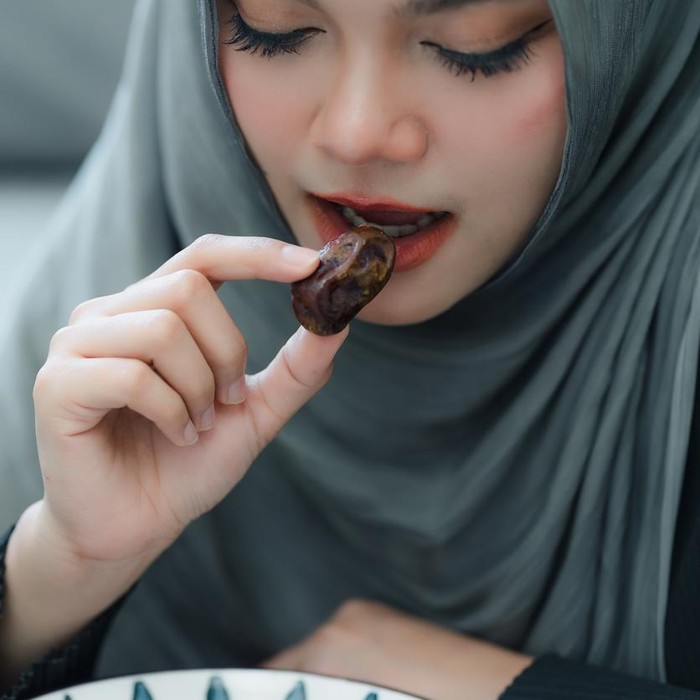 Muslim woman in hijab eating dates fruit in a comfortable home. Clouse up shot
