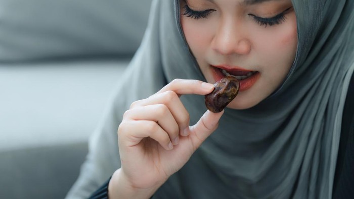 Muslim woman in hijab eating dates fruit in a comfortable home. Clouse up shot