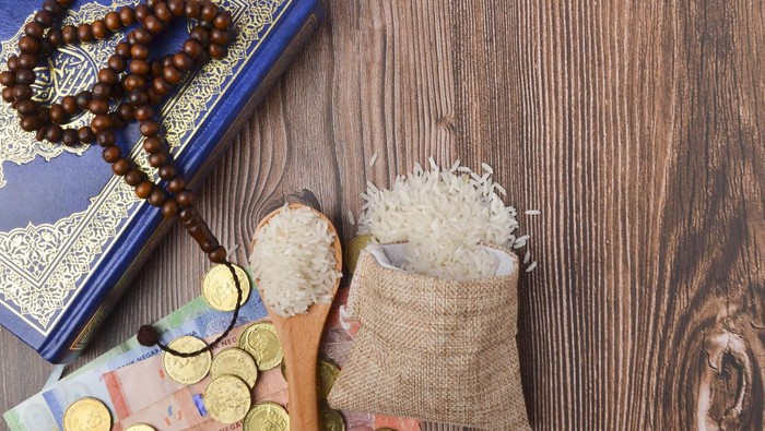Coins, rosary, Holy Quran and rice in the sack. Zakat concept. Zakat is a form of alm-giving as a religious obligation or tax. Large Arab word right method to read correctly.