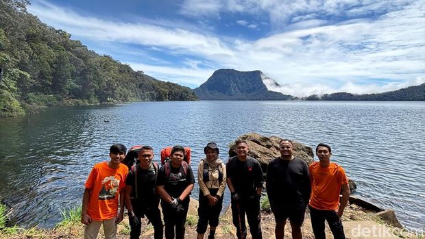 Wisatawan berfoto di pinggir Danau Gunung Tujuh dengan latar gunung yang mengelilinginya