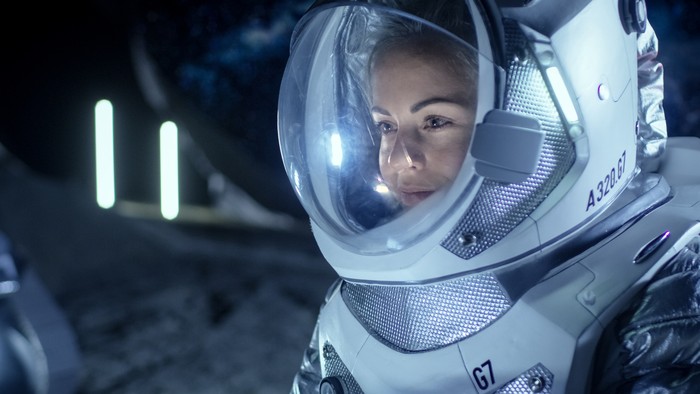 Female Astronaut Wearing Space Suit Works on a Laptop, Exploring Newly Discovered Planet, Communicating with the Earth. In the Background Her Crew Member and Living Habitat. Extraterrestrial Colonization Concept.