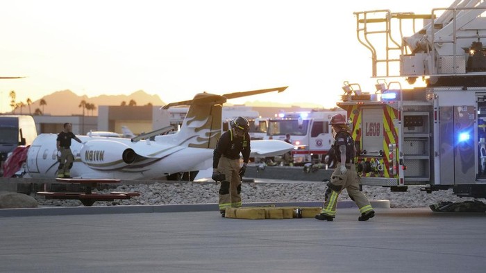 Firefighters work around the site of a crashed Learjet at Scottsdale Airport after it collided with a parked plane Monday, Feb. 10, 2025, in Scottsdale, Ariz. (AP Photo/Ross D. Franklin)