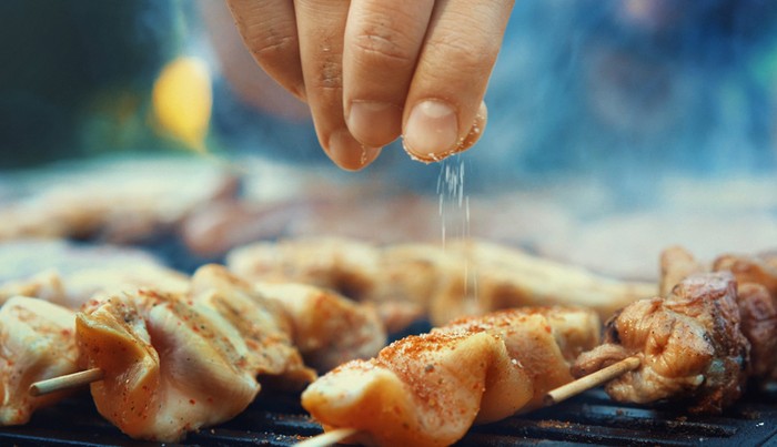 Closeup of unrecognizable male chef seasoning meat on a grill with a pinch of salt. Very shallow focus.