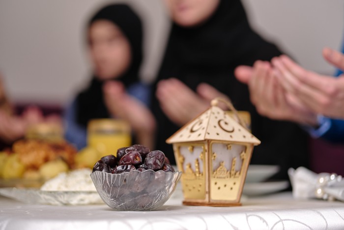 Happy Muslim family together making iftar dua to break fasting during Ramadan at the dining table at home focus on a bowl of dates. . High quality photo