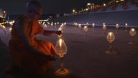 Ribuan orang berbaju putih dan biksu berjubah kuning kunyit berjalan di sekitar stupa suci Kuil Dhammakaya dekat Bangkok, memegang lilin dan melantunkan doa dalam bahasa Pali, bahasa kitab suci Buddha.  