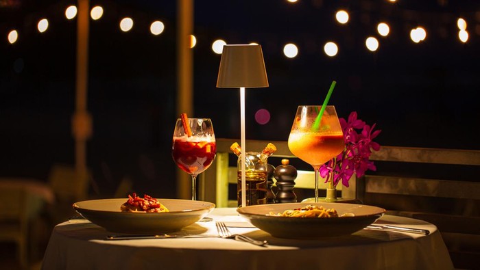 beachside dinner table,Beachside dinner table with one large challah, two bottles of red wine, two wine glasses, two tea lights in jars, one small vase with flowers, at night, with hanging light nearby in background.