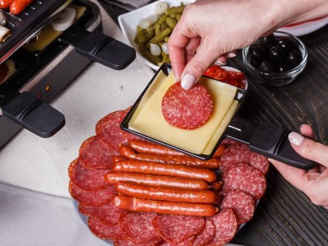young woman is preparing a traditional Swiss cheese raclette.