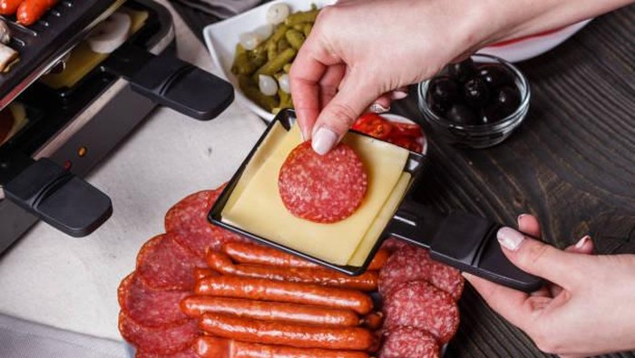 young woman is preparing a traditional Swiss cheese raclette.