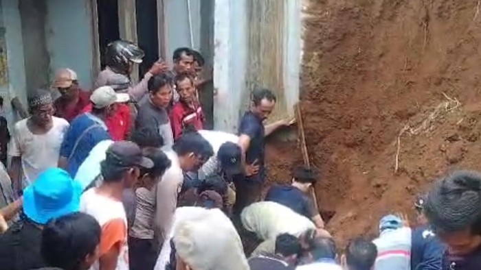 Warga mengevakuasi tukang bangunan yang tertimbun tanah longsor.