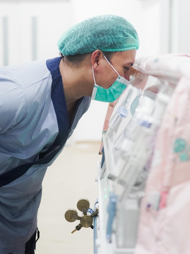 Dalam salah satu foto terlihat Rizky Febian yang masih mengenakan pakaian lengkap untuk masuk ke ruang operasi tengah melihat putri pertamanya yang baru saja lahir. Haru sekaligus bahagia tampak jelas di wajah pelantun lagu Kesempuraan Cinta tersebut. Foto: Instagram/@rizkyfbian/@mahaliniraharja