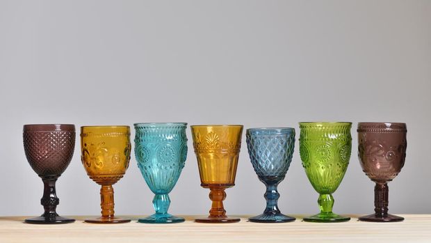 Set of empty glasses made of colored glass on gray background.