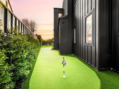 A backyard mini golf course with artificial turf next to a modern black house at sunset.