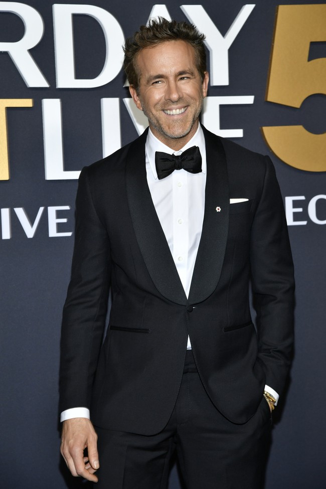 Ryan Reynolds tampil elegan dalam setelan jas hitam, lengkap dengan dasi kupu-kupu. Senyum semringah menghiasi wajahnya kala berpose di depan kamera. Foto: Evan Agostini/Invision/AP