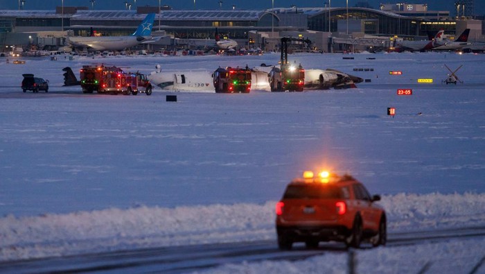 Potret Badan Pesawat Delta Air Lines Terbalik gegara Kecelakaan Emergency responders walk around a plane on a runway, after a plane crash at Toronto Pearson International Airport in Mississauga, Ontario, Canada February 17, 2025. REUTERS/Cole Burston