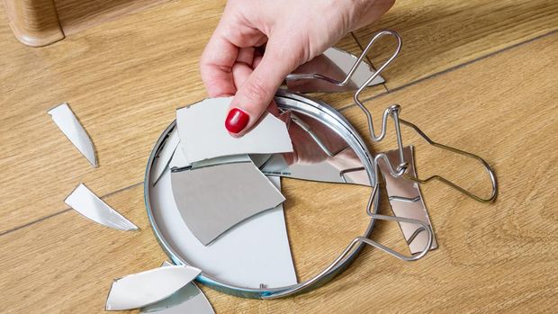Woman's hand removes broken pieces of mirror from wooden floor at home