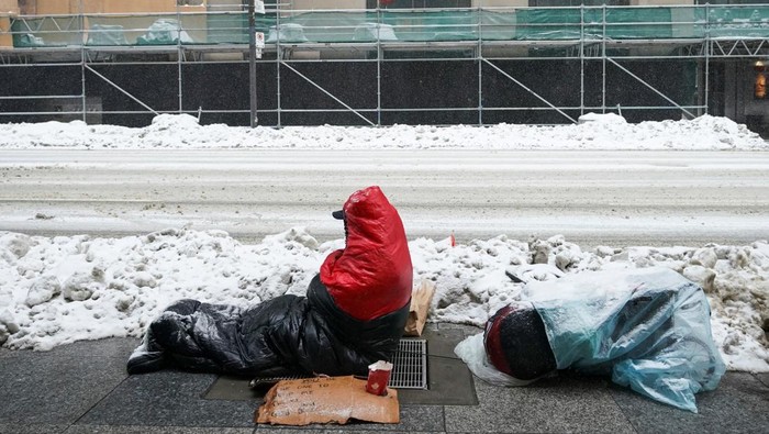 A person sits on a warm grate on the sidewalk of a snow covered street during a snowstorm in Toronto, Ontario, Canada February 15, 2025.  REUTERS/Arlyn McAdorey
