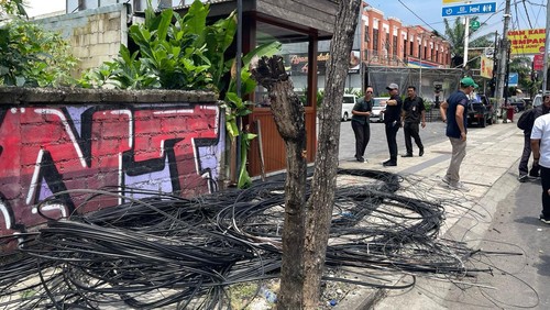 Tim PJUT Dinas PUPR Badung membersihkan kabel provider liar di Jalan Dewi Sri, Kuta, Rabu (19/2/2025). (Foto: Dok. Pemkab Badung)