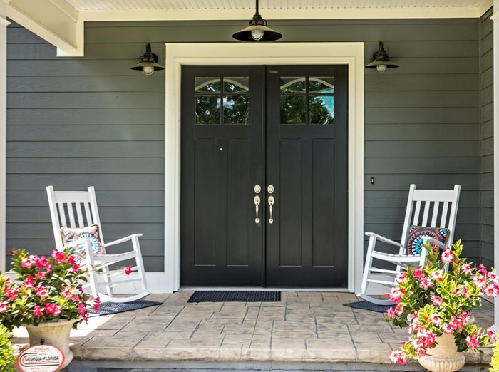 A front porch with two rocking chairs, stamped concrete floors, and double glass doors.