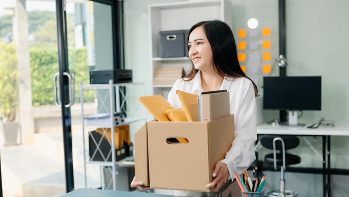 Happy and excited young beautiful Asian woman office worker celebrating her resignation, carrying her personal stuff. leaving job, changing or company.in modern office