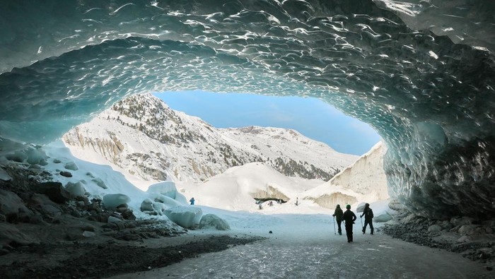 Menyusuri Dinginnya Gua Es di Swiss Hikers walk out of one of the ice caves formed by water during the summer on the tongue the Morteratsch glacier as it melts due to climate change in Pontresina near Saint Moritz in eastern Switzerland, February 21, 2025. REUTERS/Denis Balibouse