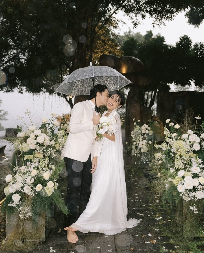 Hujan yang menemani, membuat suasana pernikahan Gregoria dan Mikha kian romantis. Keduanya hanyut dalam sukacita dan terlihat melepas sepatu untuk menikmati cuaca hari itu. Foto: dok. Instagram @venemapictures