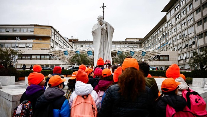 Orang-orang Berdoa untuk Kesembuhan Paus Fransiskus Children make a prayer for Pope Francis, next to the statue of late Pope John Paul II outside the Gemelli Hospital where Pope Francis is admitted to continue treatment for his ongoing respiratory tract infection, in Rome, Italy, February 19, 2025. REUTERS/Yara Nardi