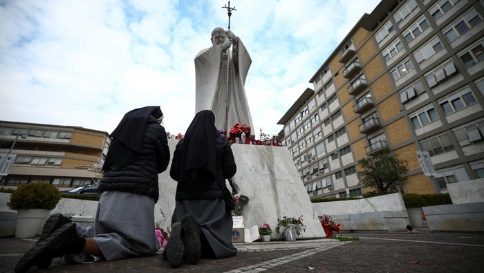 People pray next to the statue of late Pope John Paul II outside the Gemelli Hospital where Pope Francis is admitted for treatment, in Rome, Italy, February 20, 2025. REUTERS/Guglielmo Mangiapane
