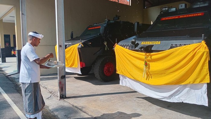 Penyelenggara ritual upacara memercikan air suci atau tirta ke mobil Todak dan Barracuda saat ritual Tumpek Landep di Mako Brimob Polda Bali, Sabtu (22/2/2025). (Aryo Mahendro/detikBali)