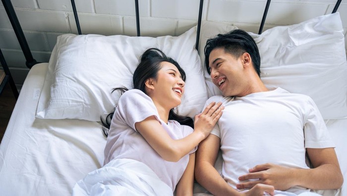 A happy young Asian couple in pajamas is enjoying watching television or a movie together in bed. couple and domestic life concepts