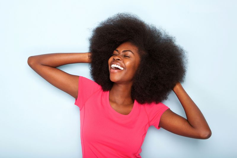 Close up portrait of cheerful young black woman with hands behind head