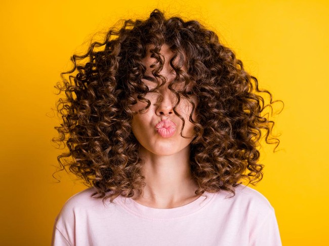 Headshot of girl with curly hairstyle wearing t-shirt send air kiss pouted lips isolated on vivid yellow color background.
