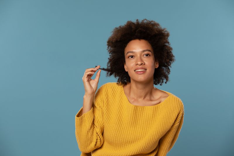 Portrait of a beautiful African American woman with curly hair in her 30s and  wearing no make up with blue background in yellow sweater stock photo
