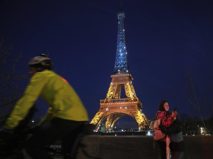 Ukrainians hold Ukrainian and European flag as the Eiffel Tower is illuminated with the colors of Ukraine to mark the third anniversary of Russias invasion of the country, in Paris, Monday, Feb. 24, 2025. (AP Photo/Christophe Ena)