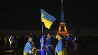 Warga Ukraina memegang bendera Ukraina dan Eropa saat Menara Eiffel diterangi dengan warna Ukraina untuk menandai ulang tahun ketiga invasi Rusia ke negara itu, di Paris, Senin (24/2/2025).  