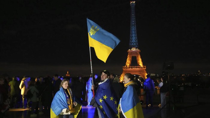 Ukrainians hold Ukrainian and European flag as the Eiffel Tower is illuminated with the colors of Ukraine to mark the third anniversary of Russia's invasion of the country, in Paris, Monday, Feb. 24, 2025. (AP Photo/Christophe Ena)