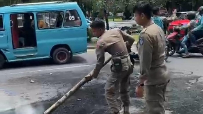 Anggota Satpol PP membersihkan bekas ban dibakar dari aksi demo di depan Kantor Gubernur Sulsel.