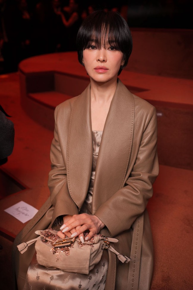 Bintang drama Korea The Glory itu mengenakan silk mini dress dan long pants abu-abu di balik leather coat coklat. Untuk melengkapi penampilannya, Song Hye Kyo menjinjing hand bag Fendi bermotif floral. Foto: Getty Images