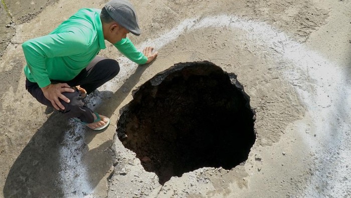 Warga yang penasaran melihat dari dekat lubang sinkhole yang terbentuk di tengah ruas jalan raya jalan selingkar Wilis, Tulungagung, Jawa Timur, Kamis(27/2/2025). Badan jalan di jalur menuju objek wisata Jurang senggani, lereng Gunung itu amblas dengan kedalaman yang belum diketahui, membentuk kawah kecil berdiameter 80 cm diduga akibat munculnya aliran air ke bawah atau ke arah perut bumi. ANTARA FOTO/Destyan Sujarwoko/foc.