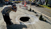 Warga yang penasaran melihat dari dekat lubang sinkhole yang terbentuk di tengah ruas jalan raya jalan selingkar Wilis, Tulungagung, Jawa Timur, Kamis(27/2/2025).