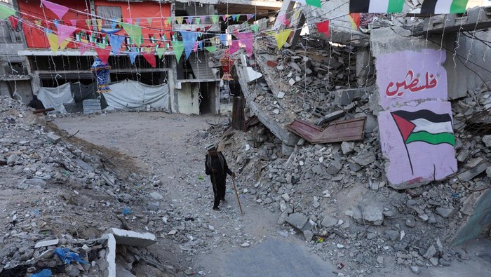 A Palestinian walks past graffiti and the rubble of buildings, ahead of the holy fasting month of Ramadan, amid a ceasefire between Israel and Hamas, in Khan Younis, in the southern Gaza Strip, February 27, 2025. REUTERS/Ramadan Abed