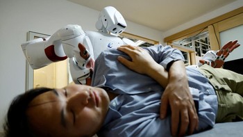 Baru-baru ini di Tokyo, sebuah robot yang digerakkan oleh AI mencondongkan tubuh ke arah seorang pria yang berbaring telentang dan dengan lembut meletakkan tangannya di lututnya dan tangan lainnya di bahunya, lalu menggulingkannya ke samping--sebuah manuver yang digunakan untuk mengganti popok atau mencegah luka baring pada orang tua.  